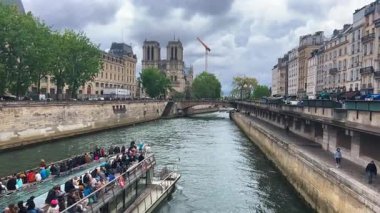 PARIS, FRANCE - 21 Nisan 2025: Seine Nehri 'nden geçen turistleri taşıyan çift güverteli feribot bulutlu bir bahar gününde Ile de la Cite' den Notre Dame Katedrali 'ne doğru yola çıkıyor..