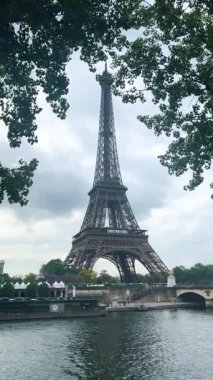 PARIS, FRANCE - 21 Nisan 2025: Seine Nehri ve Eyfel Kulesi 'nin sol kıyısındaki yeşil ağaç taçları arasındaki boşluktan bak. Dikey video.