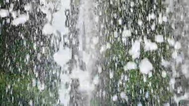 Bir yaz parkında yeşil ağaçların arka planına karşı bir çeşmenin jetleri ve damlaları. Yavaş çekim.