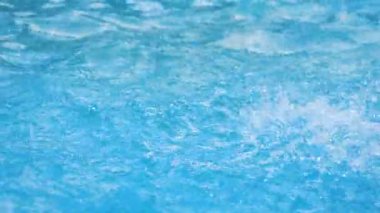 Su damlaları suyun mavi yüzeyine düşer ve sıçramalar yaratır. Yavaş çekim.