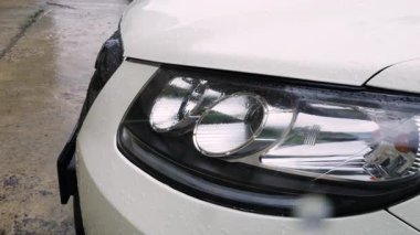 Yağmur sırasında su damlaları bir arabanın ön farının camından süzülür..