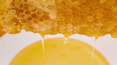 Bal peteğinden beyaz tabağa damlayan altın bal damlaları bal birikintisi oluşturuyor. Makro atış. Sağlıklı yeme kavramı.