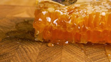 Tahta bir meşe ağacının ucunda, kaşıkla kesilmiş bir tahtanın üzerinde duran tarağın içindeki bir parça altın balı kırmak. Balmumu hücrelerine yakın çekim. Sağlıklı yeme kavramı.