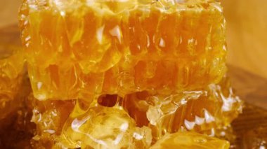 Altın bal akıntıları damlar ve meşe ağacından yapılmış tahtanın ucunda duran bal peteğinin üzerine dökülür. Balmumu bal peteklerine yakın çekim. Sağlıklı yeme kavramı.