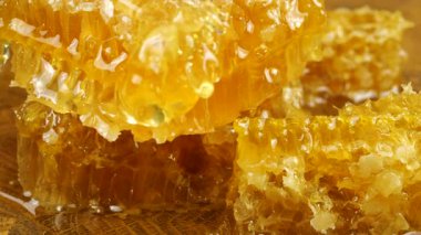 Altın bal akıntıları damlar ve meşe ağacından yapılmış tahtanın ucunda duran bal peteğinin üzerine dökülür. Balmumu bal peteklerine yakın çekim. Sağlıklı yeme kavramı.