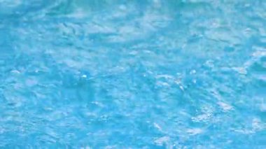 Su damlaları suyun mavi yüzeyine düşer ve sıçramalar yaratır. Yavaş çekim.