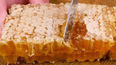 Bal peteğinin üst katmanını bıçakla kesiyor. Balmumu bal peteklerini ahşap meşe uçlu tahıl kesme tahtasına yakın çekim. Sağlıklı yeme kavramı.