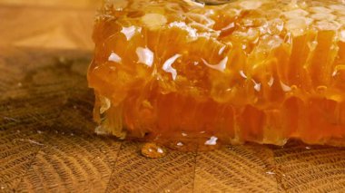 Tahta bir meşe ağacının ucunda, kaşıkla kesilmiş bir tahtanın üzerinde duran tarağın içindeki bir parça altın balı kırmak. Balmumu hücrelerine yakın çekim. Sağlıklı yeme kavramı.