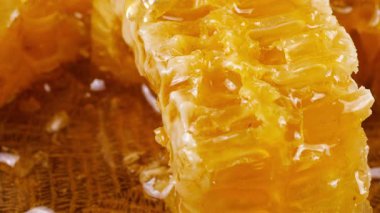 Altın bal akıntıları damlar ve meşe ağacından yapılmış tahtanın ucunda duran bal peteğinin üzerine dökülür. Balmumu bal peteklerine yakın çekim. Sağlıklı yeme kavramı.