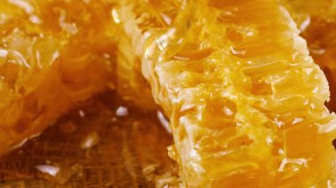 Altın bal akıntıları damlar ve meşe ağacından yapılmış tahtanın ucunda duran bal peteğinin üzerine dökülür. Balmumu bal peteklerine yakın çekim. Sağlıklı yeme kavramı.