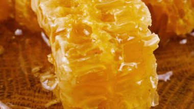Altın bal akıntıları damlar ve meşe ağacından yapılmış tahtanın ucunda duran bal peteğinin üzerine dökülür. Balmumu bal peteklerine yakın çekim. Sağlıklı yeme kavramı.