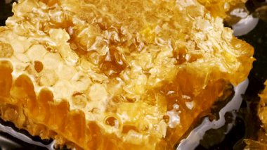 Ballı bal peteği parçaları siyah bir taş servis tahtasının üzerinde dönüyor. Balmumu hücrelerini arı balı ile kapatın. Sağlıklı yeme kavramı.