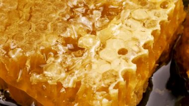 Ballı bal peteği parçaları siyah bir taş servis tahtasının üzerinde dönüyor. Balmumu hücrelerini arı balı ile kapatın. Makro atış. Sağlıklı yeme kavramı.