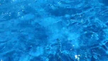 Parlak güneşli bir günde mavi suyun berrak yüzeyinde hafif dalgalar olur..