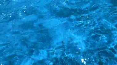 Parlak güneşli bir günde mavi suyun berrak yüzeyinde hafif dalgalar olur..