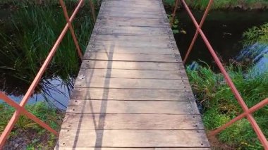 Göletin üzerinde metal parmaklıklar olan tahta bir köprü..