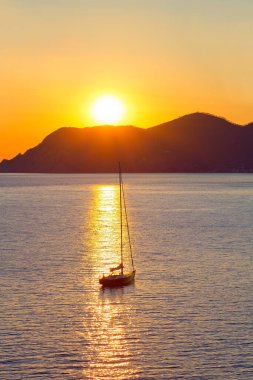 Akdeniz 'de gün batımında yelkenli yelkenliyle yelkenliyle yelken açan yat, denizde beyaz yelkenli yelkenli.