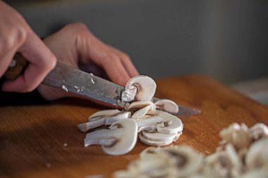 female hand cut with a sharp knife thin slices of gibs of champignons on a cutting board. To coo