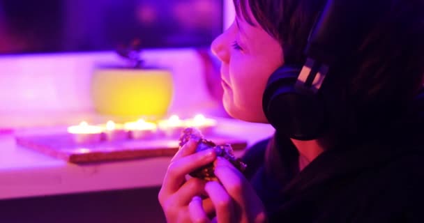 ヘッドフォンの幸せな男の子は音楽を楽しむチョコレートドーナツを食べる — ストック動画