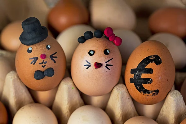 two cute hare eggs in a black hat and with a red plasticine bow in an egg container with a drawn euro egg. Rise in price. Easte