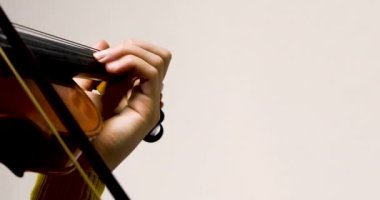 left hand of a young violinist on the strings on a student's violin on a light background. Musical education