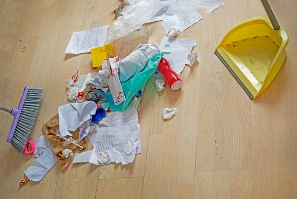 teenage girl cleans up the trash in her room with a broom and a dustpan on the parquet