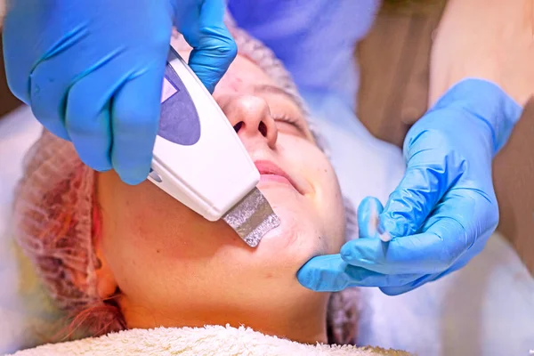 beautician cleans the face of a young girl with a laser, horizontal