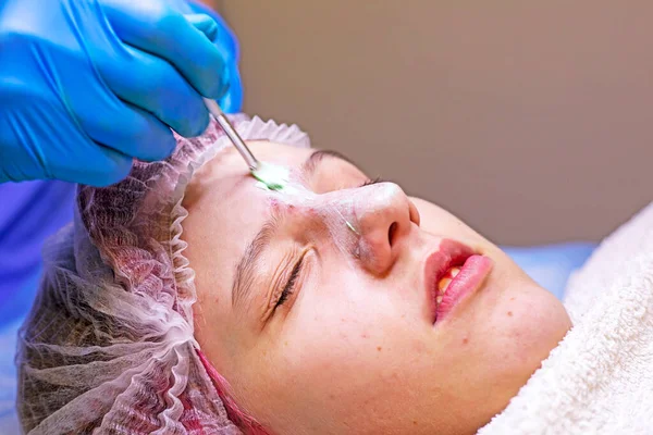 stock image cosmetologist applies a medical mask with a brush on the nose of a young girl. horizontal