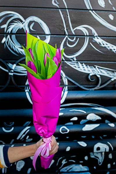 boy gives a bouquet of lilac tulips in purple paper on an abstract black and white background. Mother's day, women's day. Vertical