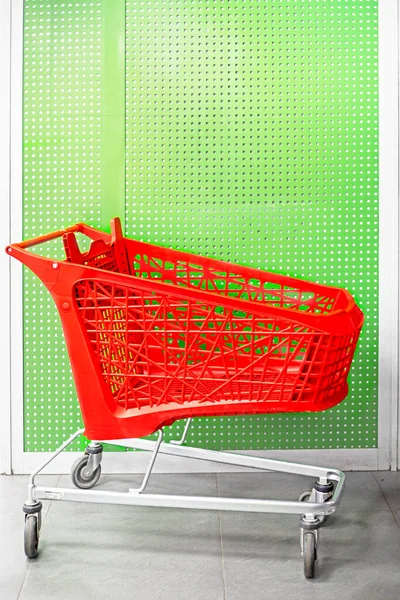 empty red cart for groceries in the mall on near the green wall.