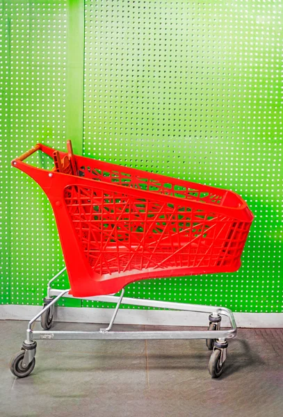 red cart for groceries in the mall on near the green wall. vertical