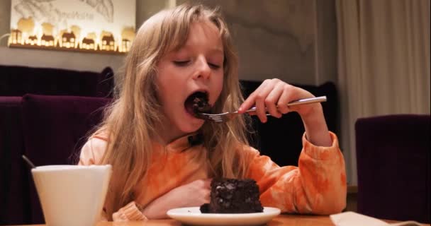 Девушка Длинными Светлыми Волосами Счастливо Ест Шоколадный Торт Вилкой Кафе — стоковое видео