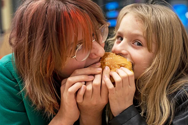 happy funny two girls bite off a small burger from two sides. horizontal