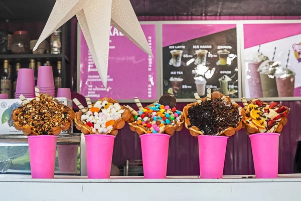 stock image showcase with different types of ice cream in waffle cones with marmesh, nuts, sweets, coconut and chocolate chips in pink cups