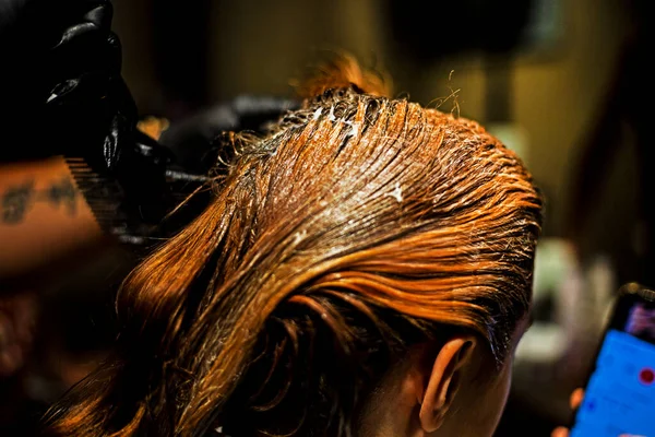 hairdresser applying paint with a brush and comb to bright red strands of hair. everyday life