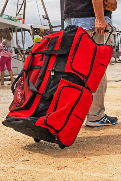 carry a huge red suitcase, a bag on wheels, to the pier to the ship. Travel and leisure