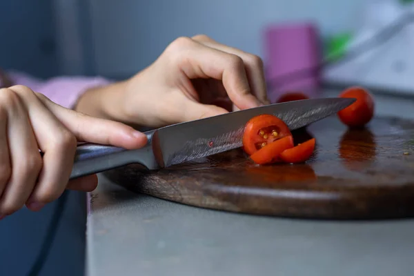 girl\'s hand holds a knife and cuts a cherry tomato into slices on a cutting board