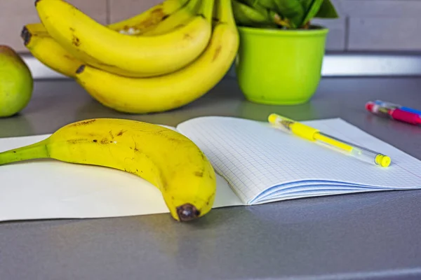 banana on the table next to a school notebook with pens. school snack