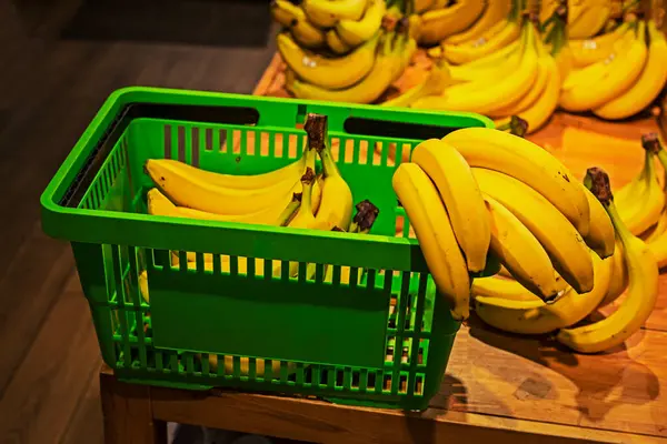 putting bananas in the green grocery basket in the supermarket