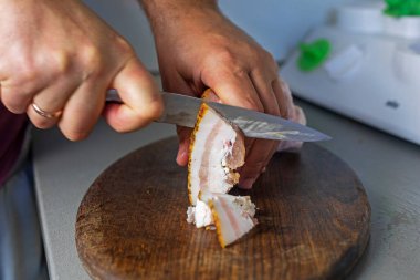 Adam bir parça pastırmayı kesme tahtasındaki bıçakla ince parçalara ayırıyor.