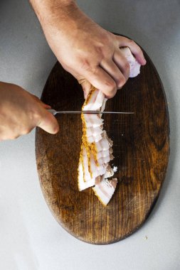 Adam bir parça pastırmayı kesme tahtasındaki bıçakla ince parçalara ayırıyor.