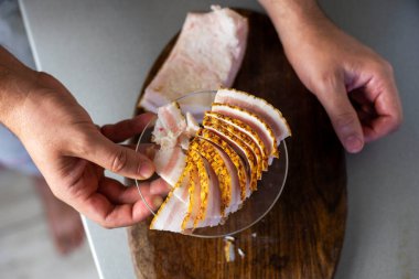 Kesme tahtasındaki ince dilimlenmiş pastırma parçalarını ve tabağa yerleştirmek için elinizi kullanın. Düz çizgi