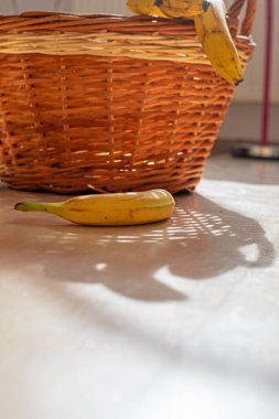 Bir demet sarı muz rattan bir sepetin yanında yatıyor.