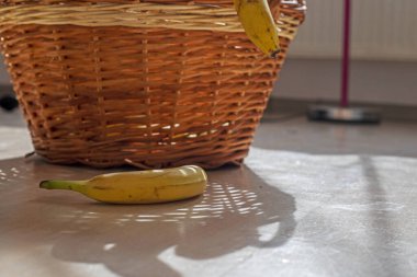 Bir demet sarı muz rattan bir sepetin yanında yatıyor.