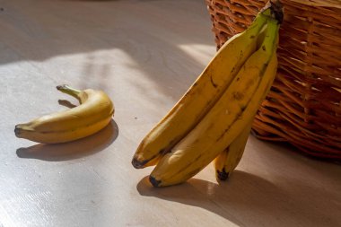 Bir demet sarı muz rattan bir sepetin yanında yatıyor.