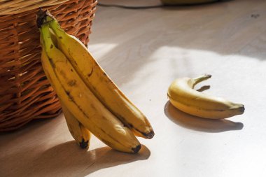 Bir demet sarı muz rattan bir sepetin yanında yatıyor.