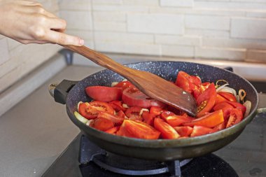Mutfakta kızartma tavasında pişirmek için özel ahşap bir spatulayla soğanlı domates karıştıran bir kız.