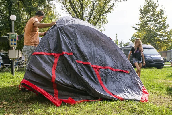 Dad and children cover a tent with an awning at a camping camp. Family holidays and traveling by car