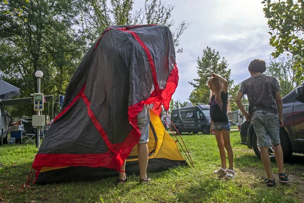 Dad and children cover a tent with an awning at a camping camp. Family holidays and traveling by car