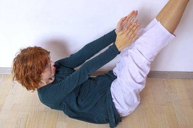 Gözlüklü genç kız duvara yakın kaslarını güçlendirmek için egzersiz yapıyor, kollarını yana kaldırıyor.